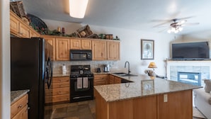 Une cuisine avec des meubles en bois, un plan de travail en granit, un réfrigérateur noir, une cuisinière, un four à micro-ondes et un évier.