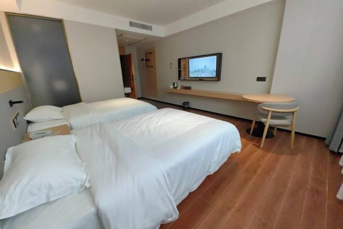 Habitación de hotel con dos camas, un televisor montado en la pared, una mesita y una silla.