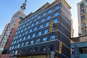 Een hotel met meerdere verdiepingen, een moderne gevel, veel ramen en een opvallend geel bord met de naam.