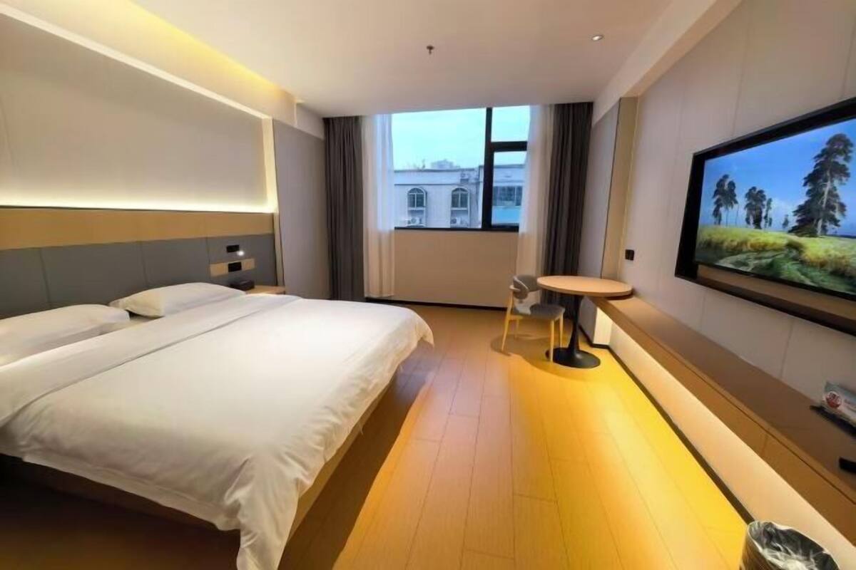 Habitación de hotel con una cama grande, una mesita, un televisor y ventana con vistas a edificios.