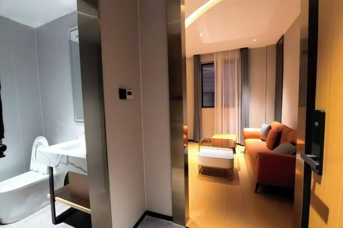 Una habitación de hotel moderna con baño, un sofá, una mesita de noche y un ventanal con cortinas.