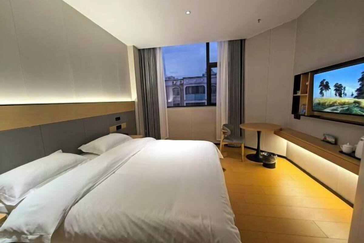 Habitación de hotel con una cama grande, un escritorio, una silla, un televisor y una ventana con vistas a edificios.