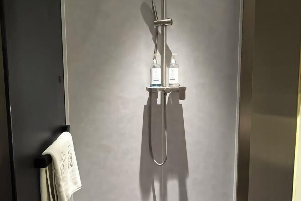 A shower with a handheld showerhead and two bottles of shampoo on a shelf.