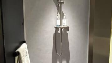 A shower with a handheld showerhead and two bottles of shampoo on a shelf.