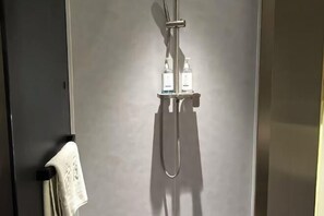 A shower with a handheld showerhead and two bottles of shampoo on a shelf.
