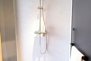A shower with a handheld hose and a wall-mounted control panel.