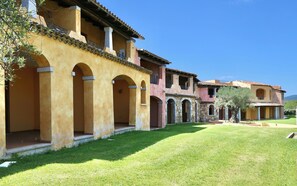 A row of traditional Mediterranean-style buildings with arched doorways and a well-maintained lawn. - Marina Beach (Golfo Aranci)