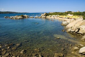 A rocky beach with clear water, large boulders, and a few people swimming. - Marina Beach (Golfo Aranci)