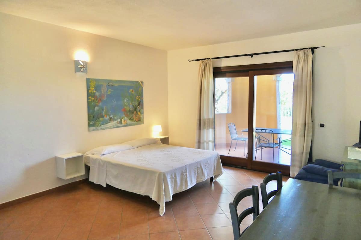 A room with a bed, a table, chairs, a painting, and a sliding glass door leading to an outdoor area.