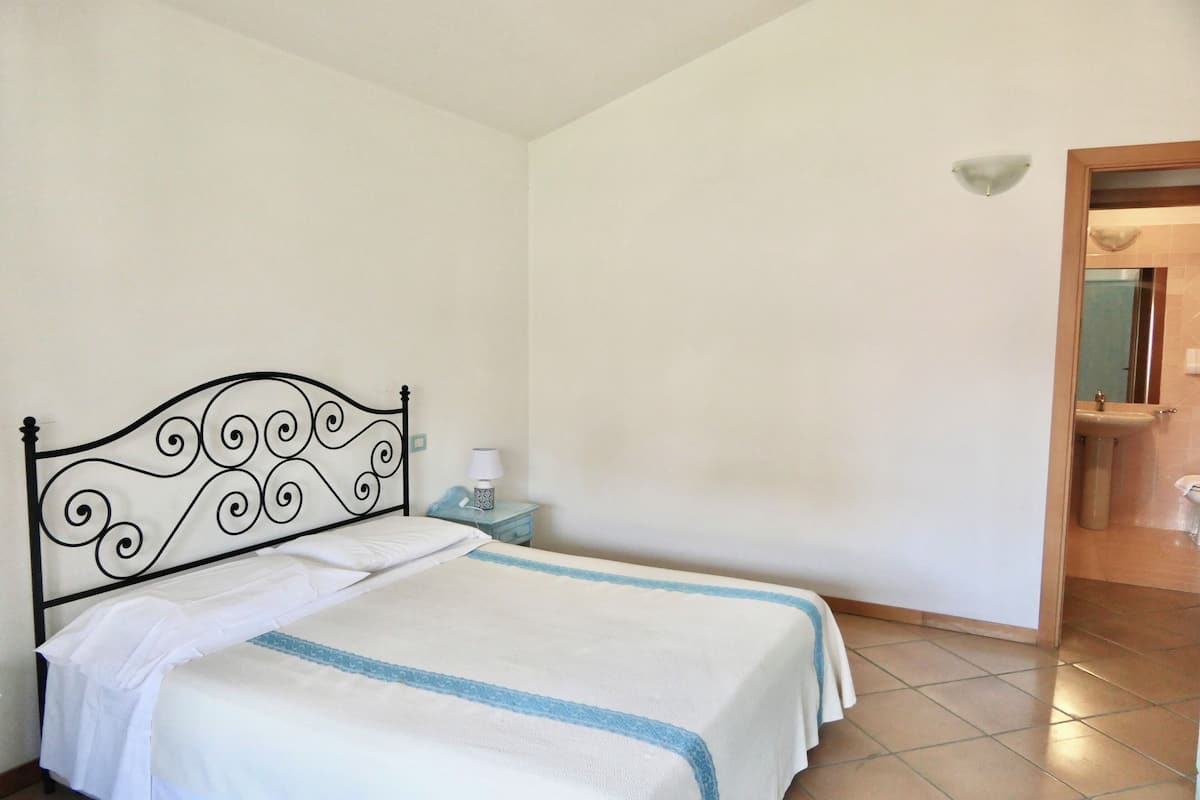 A bedroom with a bed, a nightstand, a wall-mounted light, and a bathroom door.
