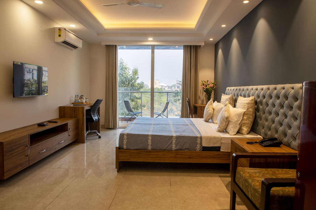 A modern bedroom with a large bed, a TV, a desk, and a balcony with a view.