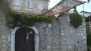 A stone wall with a dark wooden door, a sign reading "10", and a building with white shutters in the background.