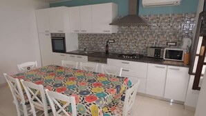 A kitchen with white cabinets, a tiled backsplash, a microwave, a stove, and a dining table with a colorful tablecloth.
