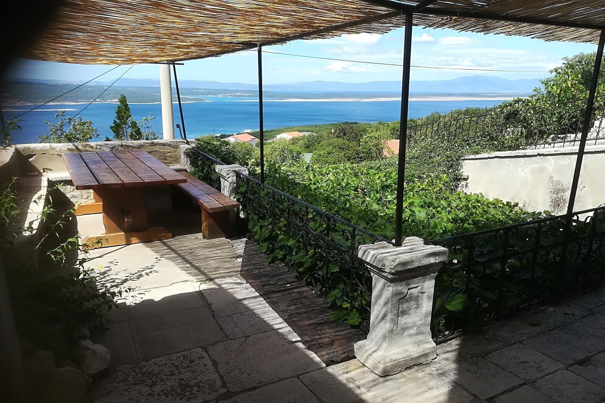 A terrace with a wooden table and benches, overlooking a scenic view of the sea and mountains.