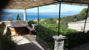 A terrace with a wooden table and benches, overlooking a scenic view of the sea and mountains.