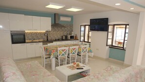 A modern kitchen with white cabinets, a tiled backsplash, and a dining area with a colorful tablecloth and white chairs.