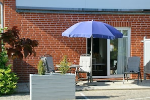 A patio with a blue umbrella, a brick building, a white chair, and a small table.