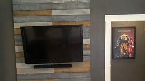 Een moderne woonkamer met een flatscreen televisie aan een houten wand, een poster van Bob Marley in een lijst en een visgraatvloer.