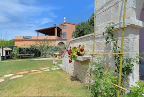 A stone wall with a climbing plant, a stone bench, and a building in the background.