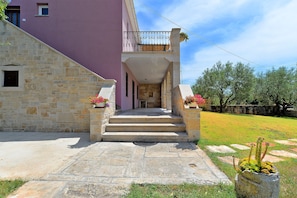 A stone staircase leading to a balcony with a wrought iron railing, surrounded by a stone wall and a grassy area with trees.