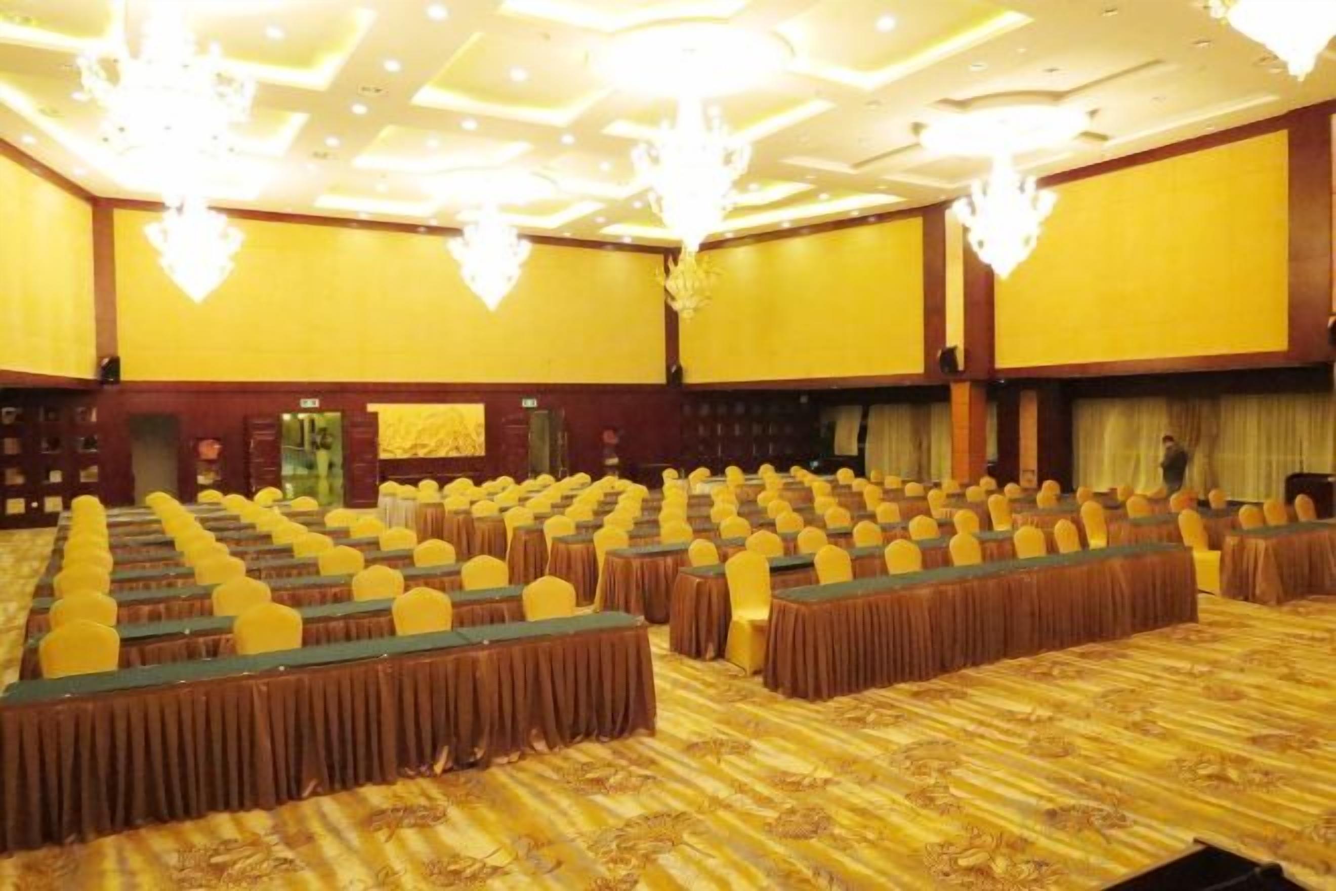 A conference room with rows of tables and chairs, a patterned carpet, and chandeliers.