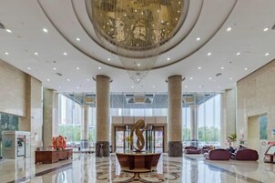 Un vestíbulo amplio con una imponente araña, grandes columnas y una mesa de recepción.