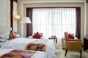 A hotel room with a bed, two chairs, a desk, and a large window with curtains.