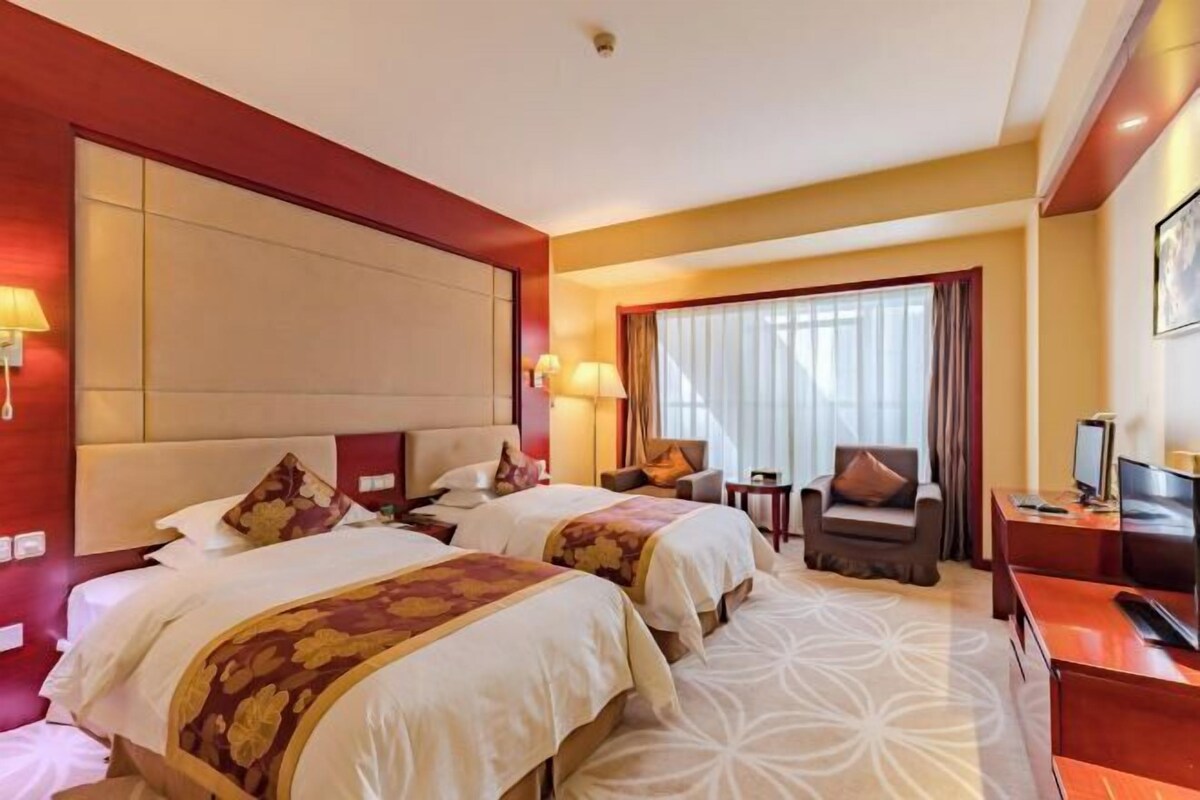 A hotel room with two beds, a desk, a chair, a TV, and a window with curtains.