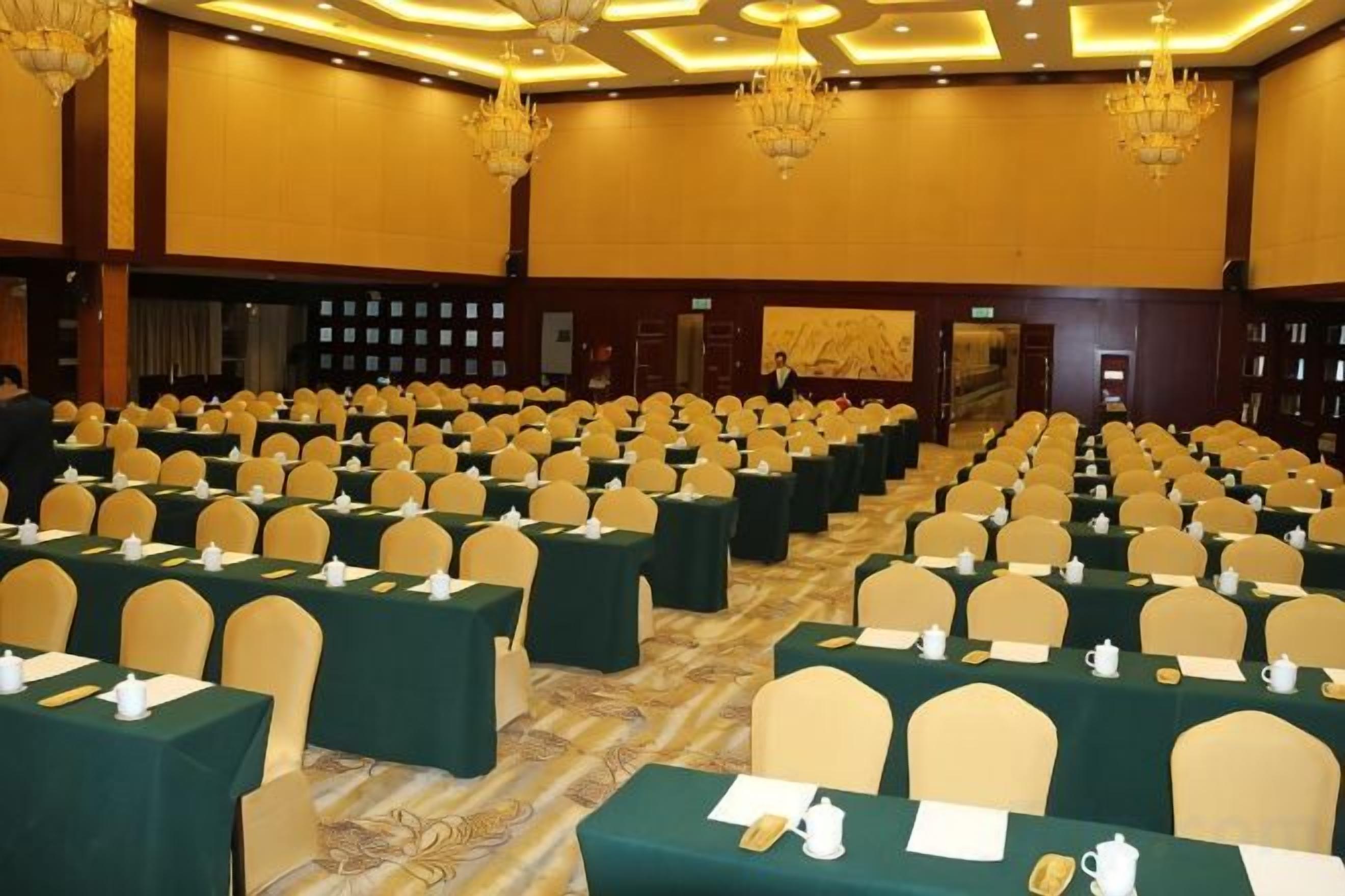 A conference room with rows of tables and chairs, a chandelier, and a carpeted floor.