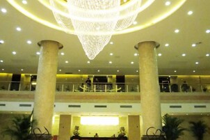 Um saguão com um lustre imponente, vários andares e um balcão de recepção.