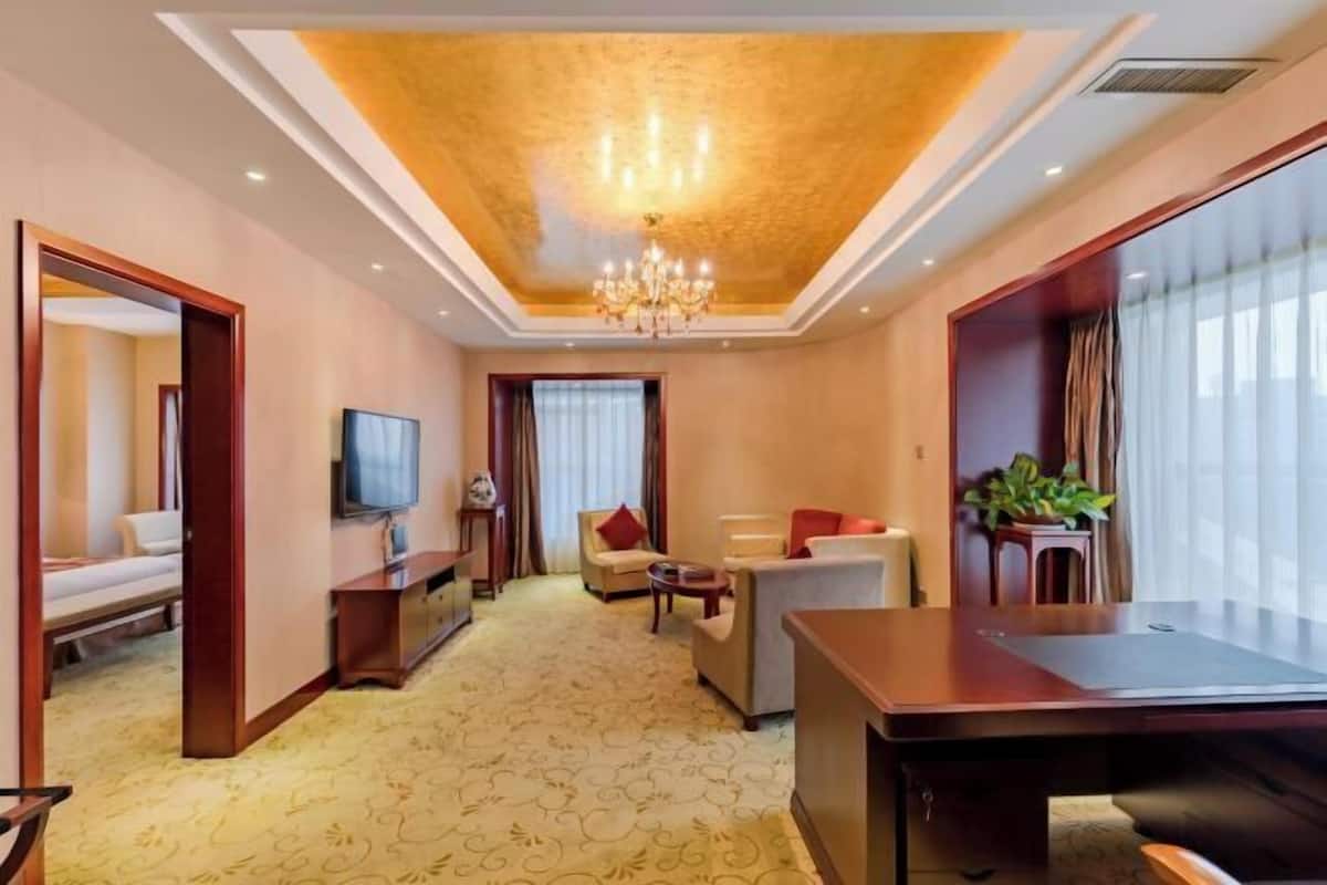 A hotel room with a large bed, a desk, a TV, and a seating area with a chandelier.