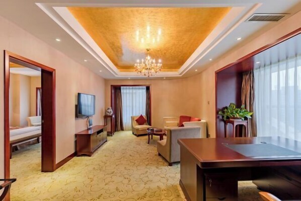 A hotel room with a large bed, a desk, a TV, and a seating area with a chandelier. - Jiu Long International Hotel (Mengcheng)