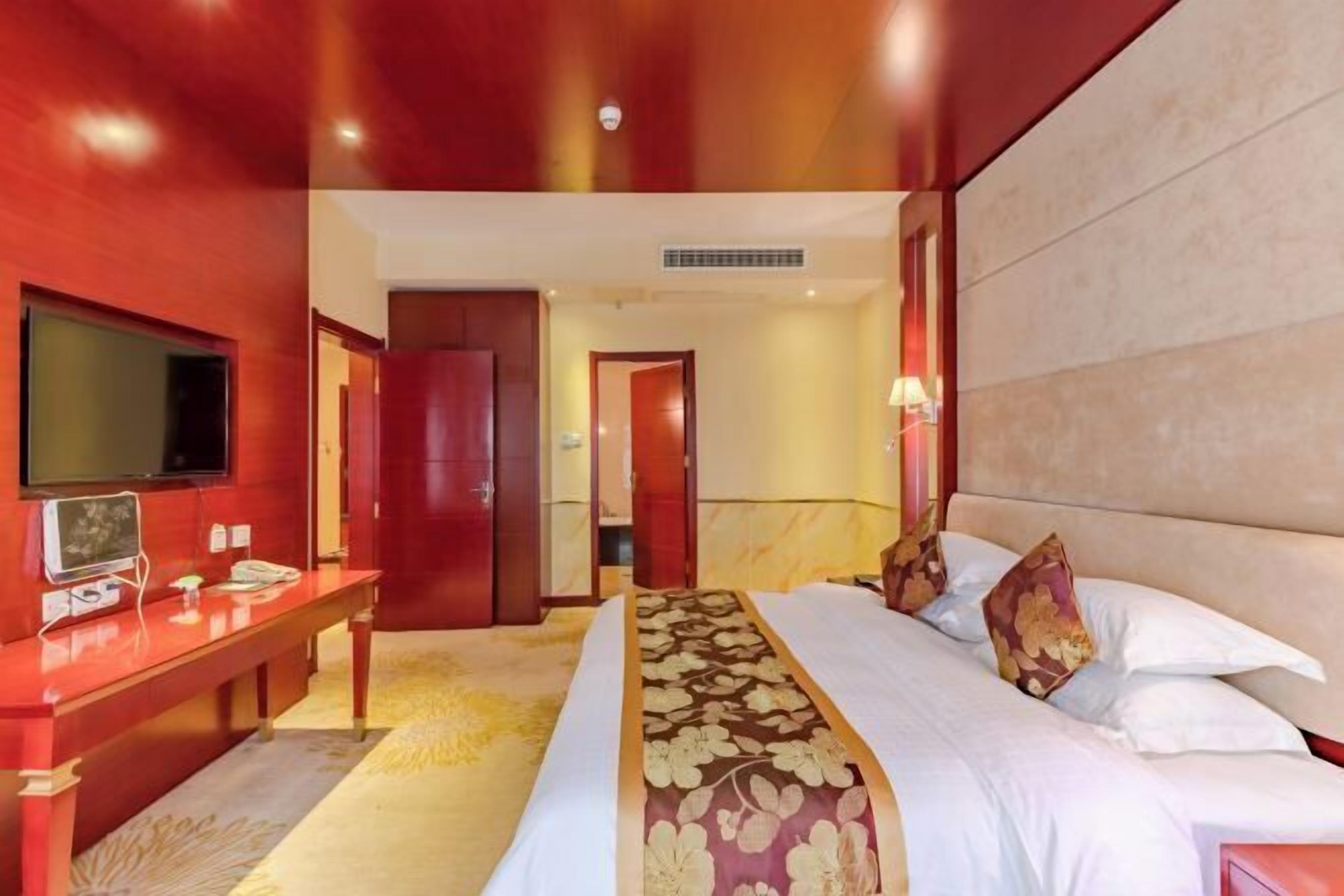 A hotel room with a large bed, a desk, a television, and a mirror.