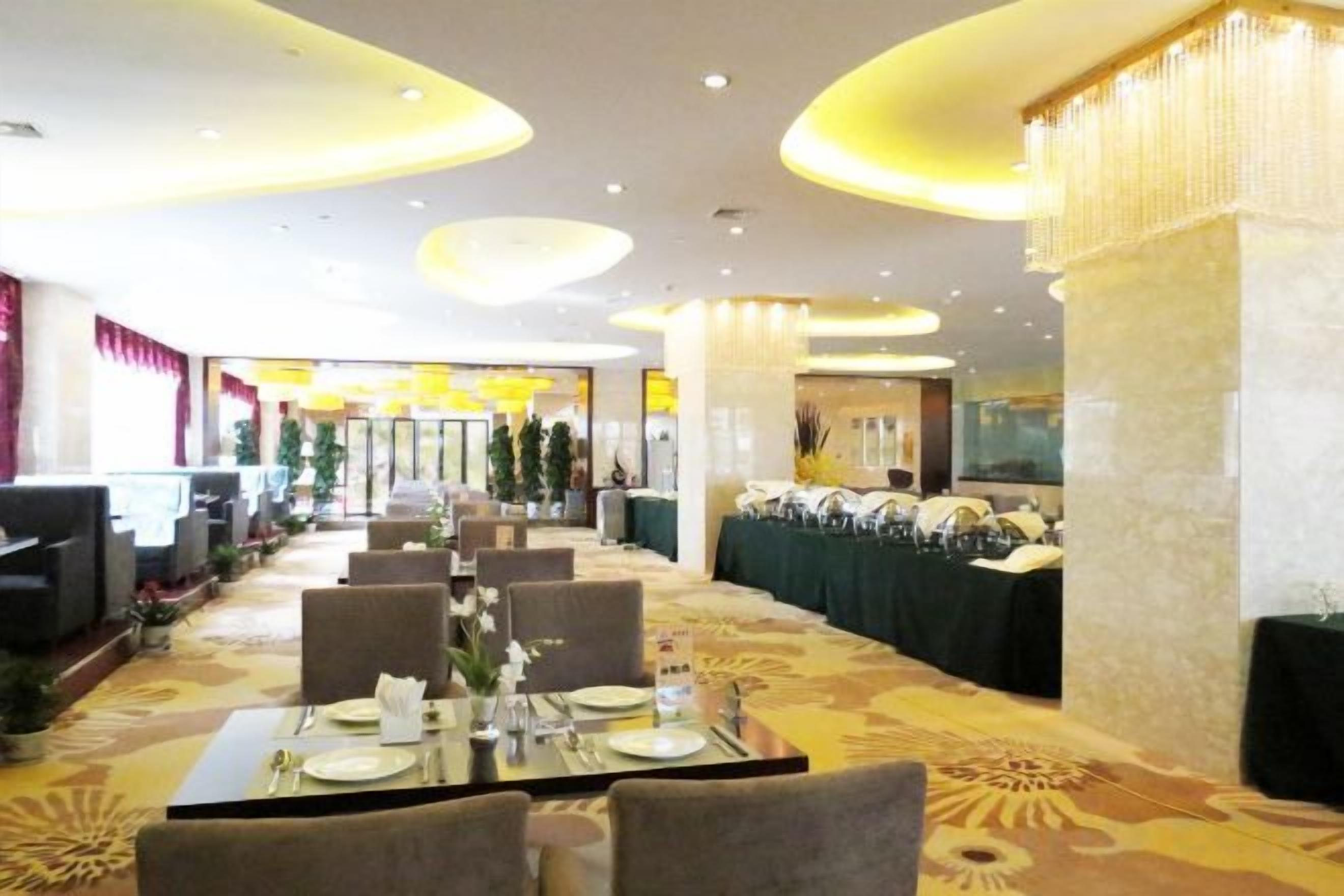 Een restaurantgedeelte in een hotel met gedekte tafels voor gasten, een kroonluchter en uitzicht op de ingang.