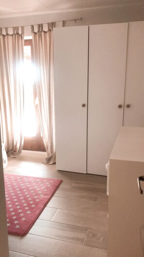 A room with a large wardrobe, a pink star-patterned rug, and a window with curtains.