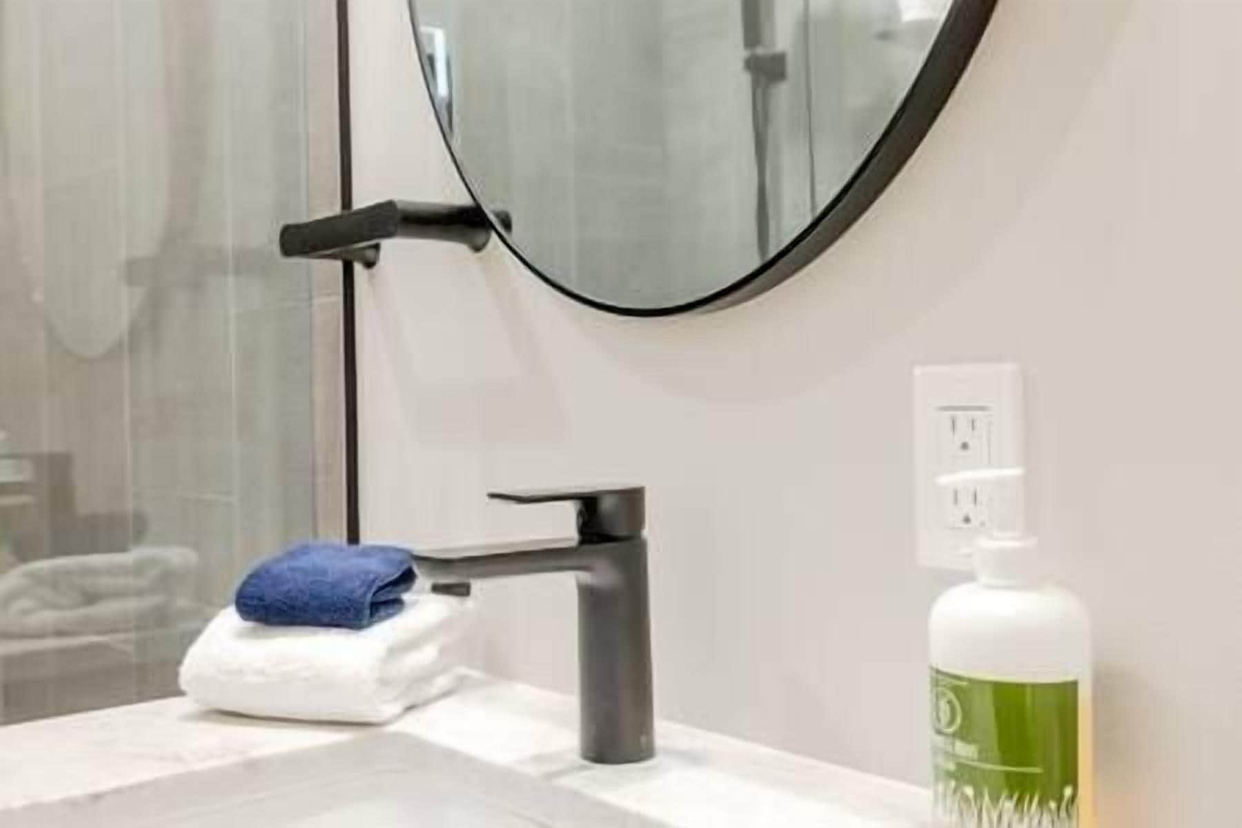Un baño con un lavamanos moderno, un espejo y una botella de jabón para las manos.