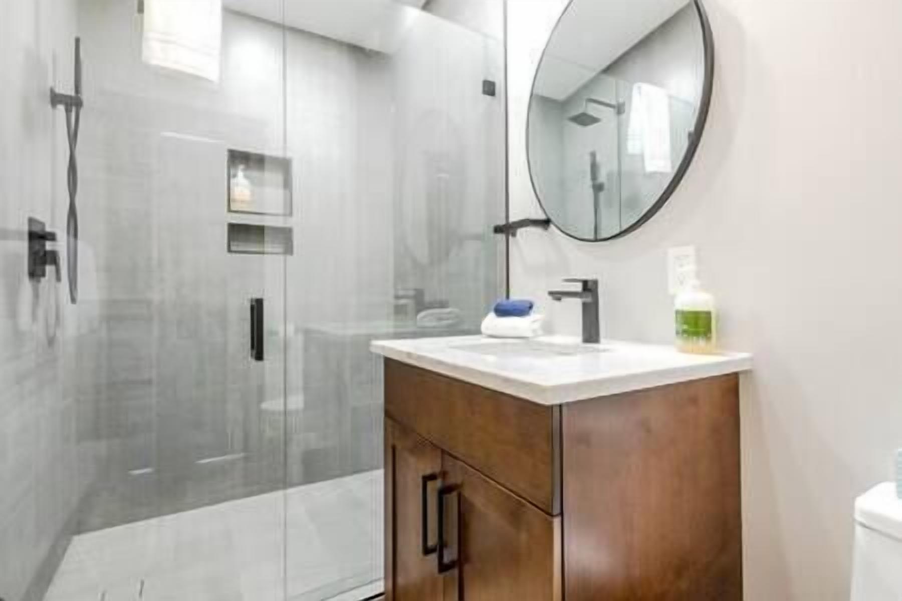 A modern bathroom with a glass shower enclosure, a wooden vanity with a mirror, and a white sink.