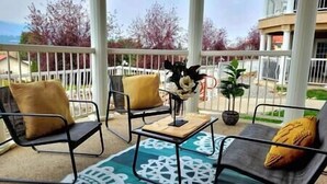 A covered outdoor seating area with two chairs and a table, a decorative rug, and a potted plant.