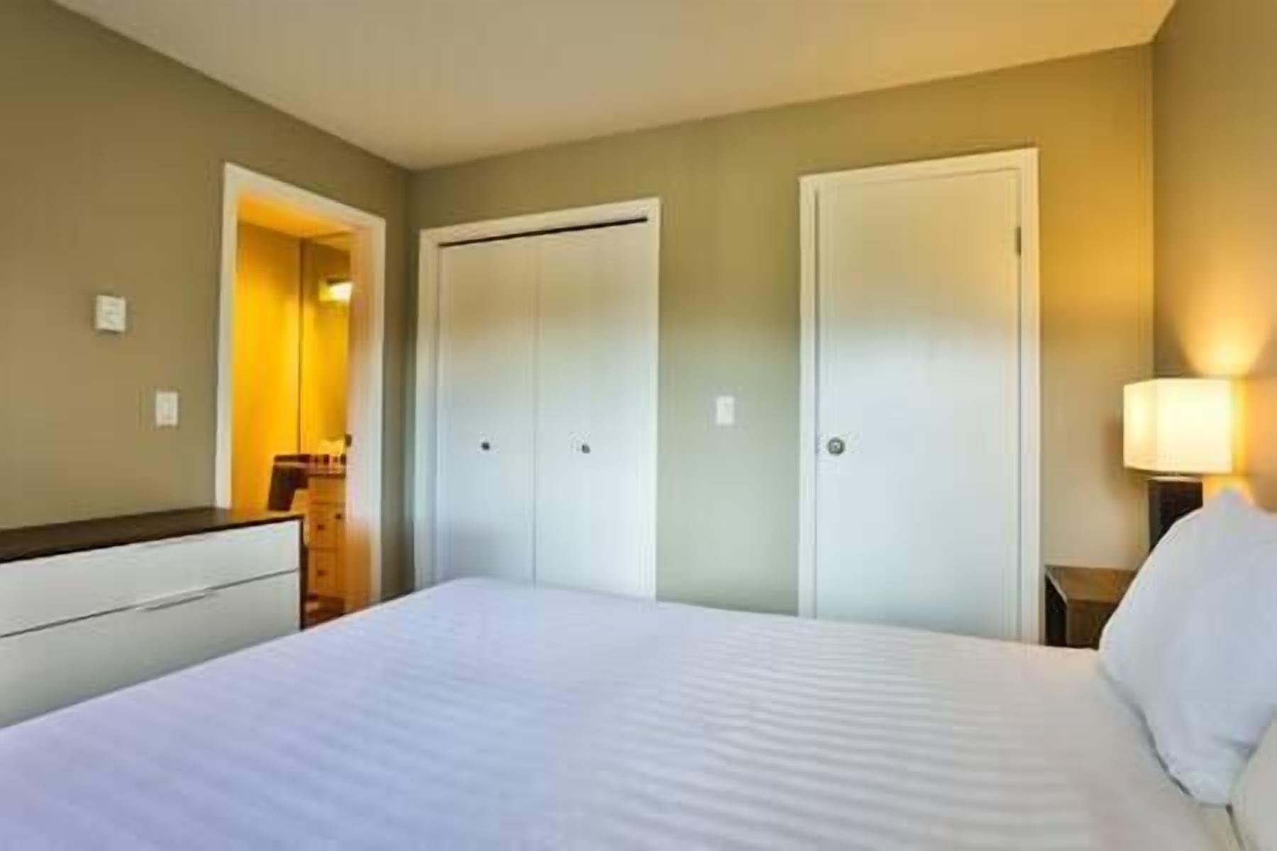 A hotel room with a bed, a dresser, and two doors.