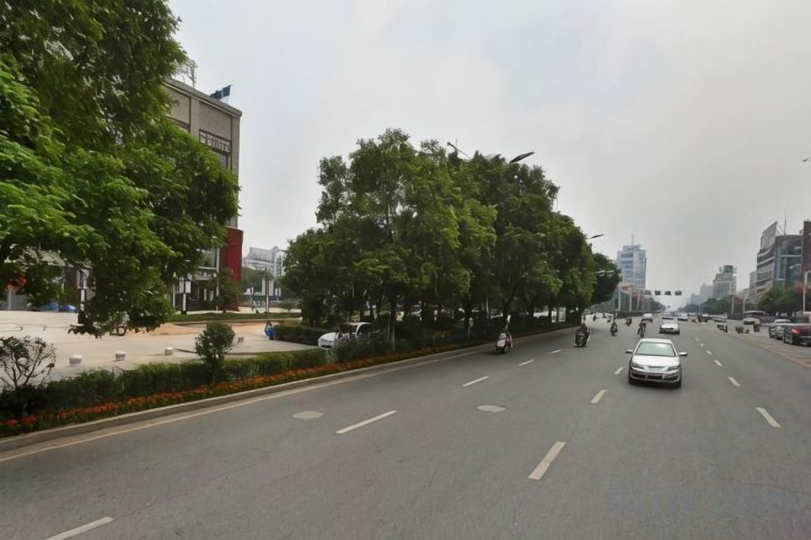 Una carretera con varios carriles, vehículos, árboles y edificios a lo largo de ella.