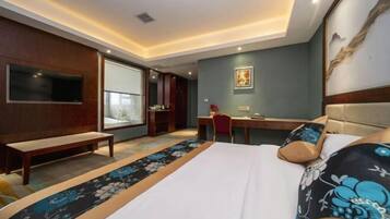 Een hotelkamer met een bed, een bureau, een stoel, een bankje, een televisie en een groot raam.