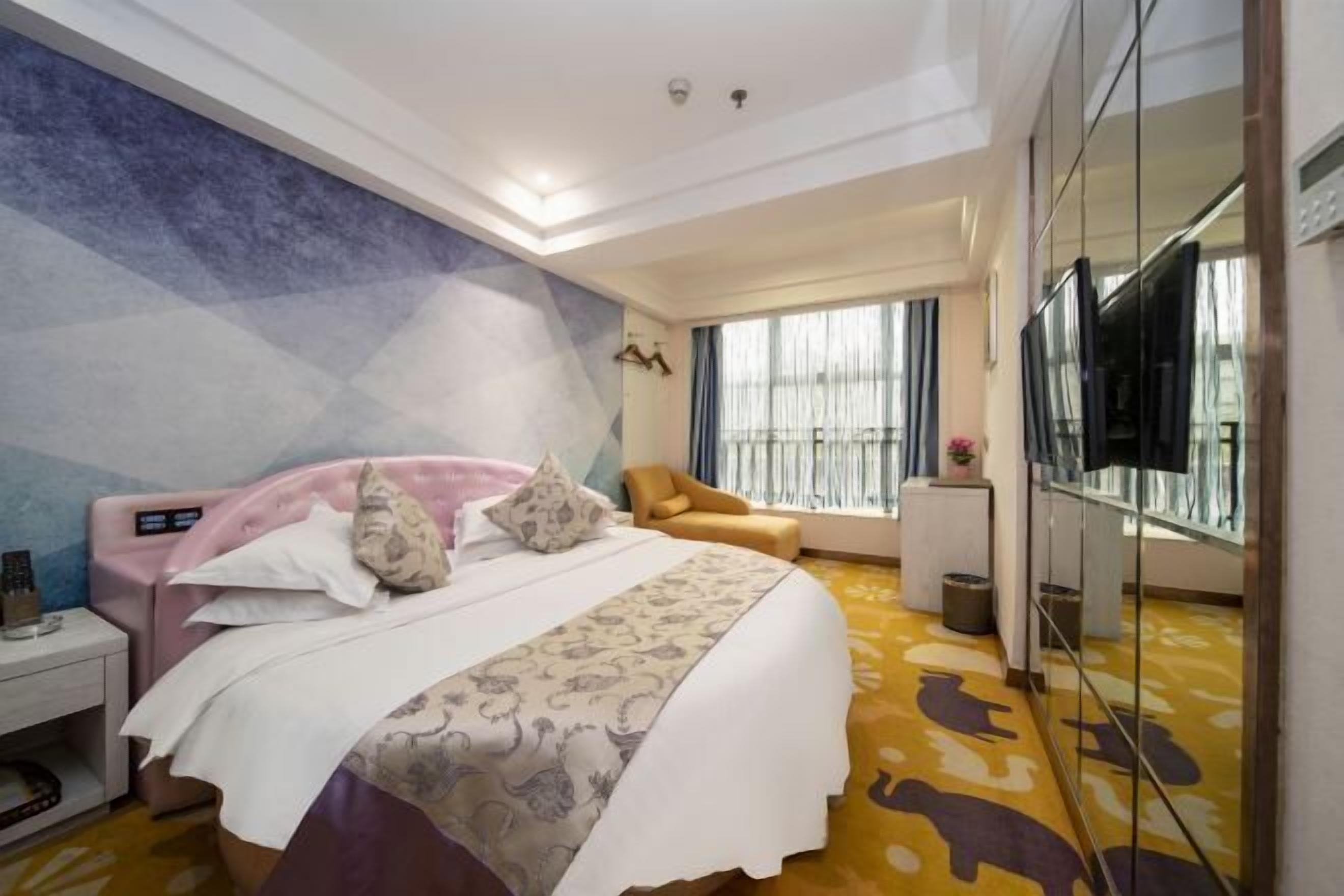 Een hotelkamer met een bed, een stoel, een televisie en een grote spiegel.