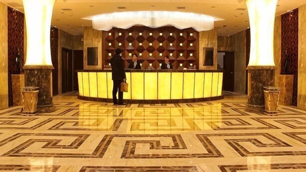 A hotel reception area with a central counter, a chandelier, and a patterned floor.