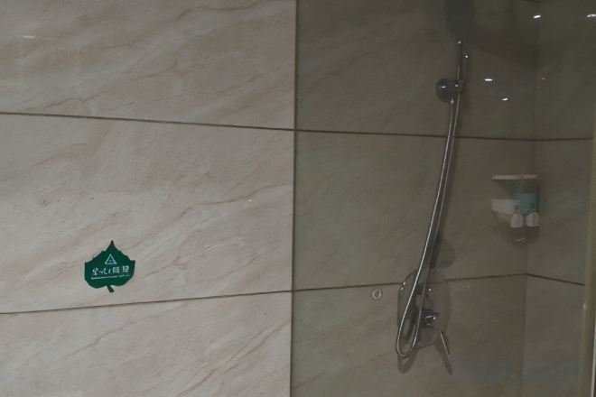 A shower with a glass enclosure, a handrail, and a soap dispenser on the wall.