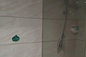Ducha con mampara de vidrio, barra de apoyo y dispensador de jabón en la pared.