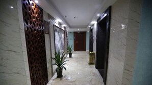 A marble-floored hallway with a decorative metal panel, potted plants, and a door at the end.