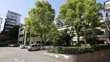 Un pàrquing amb cotxes, un edifici de diverses plantes i arbres.