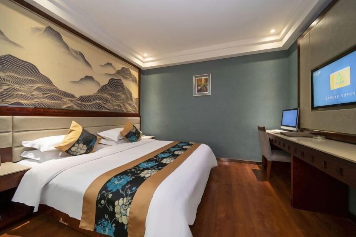 A hotel room with a bed, a desk, a television, and a wall with a decorative painting.