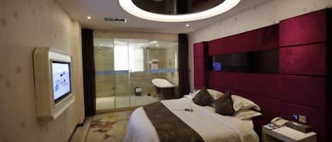 A modern hotel room with a large bed, a TV, a glass shower enclosure, and a red accent wall.