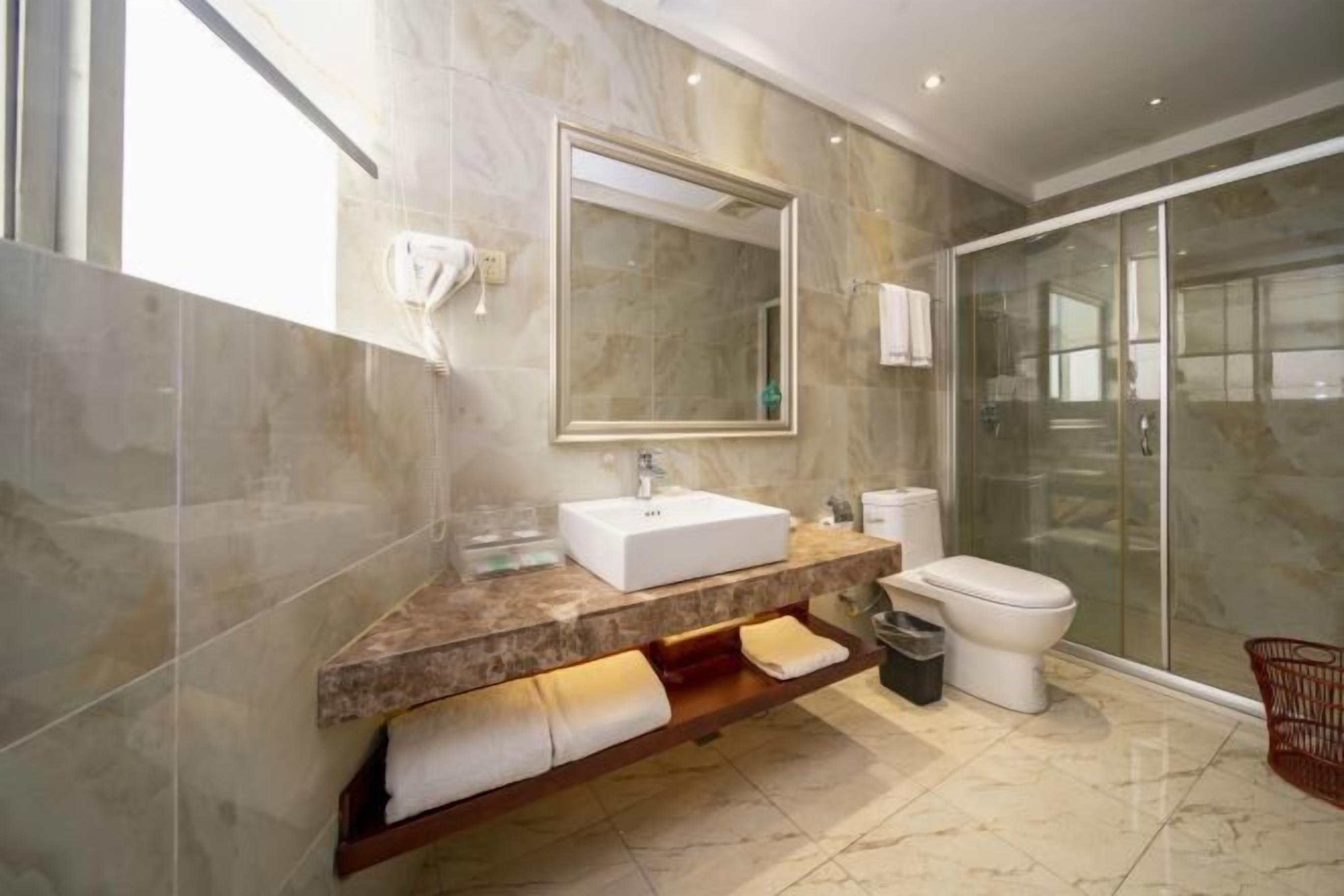Un baño moderno con tocador de mármol, un espejo grande, inodoro y cabina de ducha de vidrio.